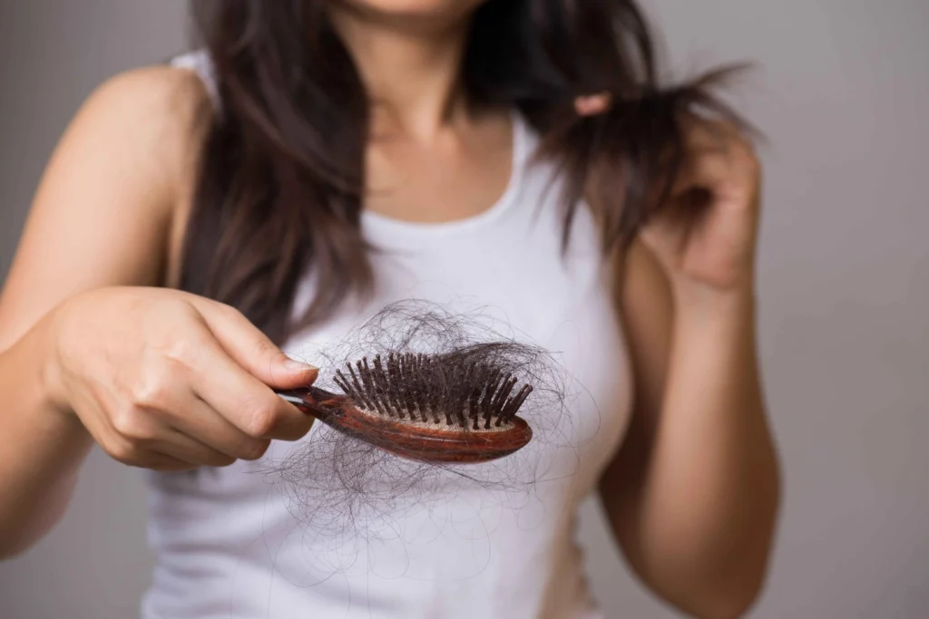 A female holding a wooden hairbrush with a large amount of lost hair and ready to get Female Hair Loss Treatment in Austin, TX with Glo Medspa